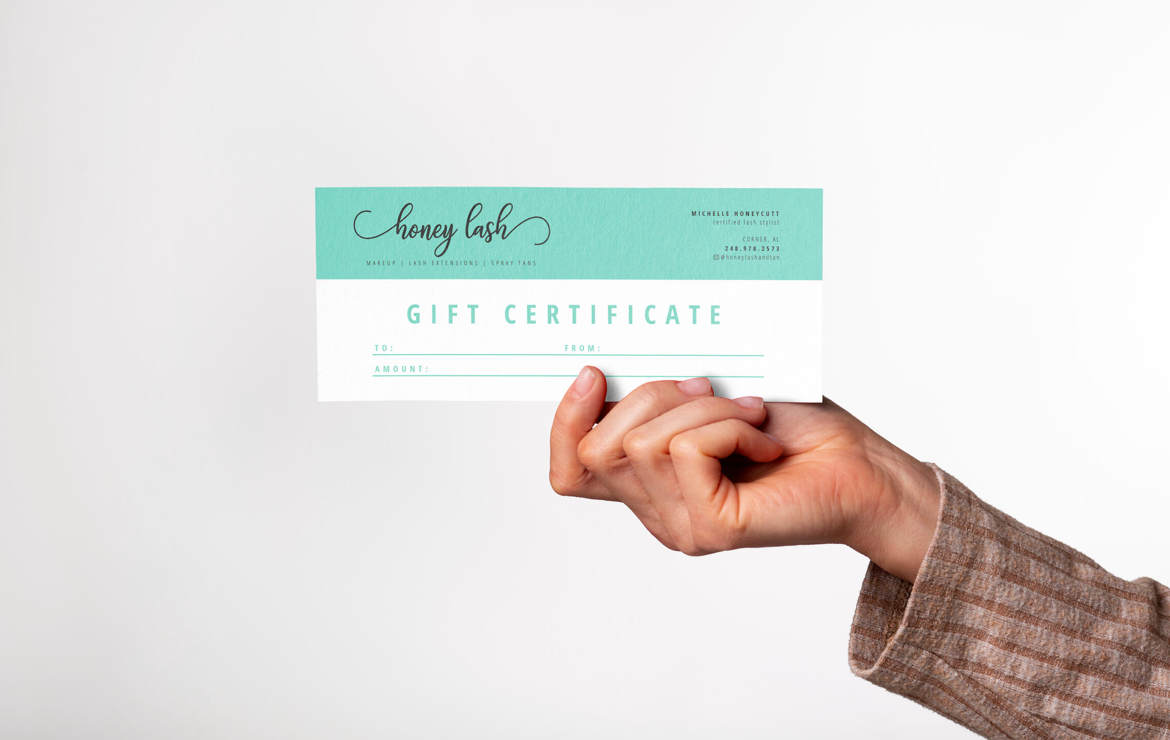 A woman's hand holding a gift certificate for Honey Lash against a white background.