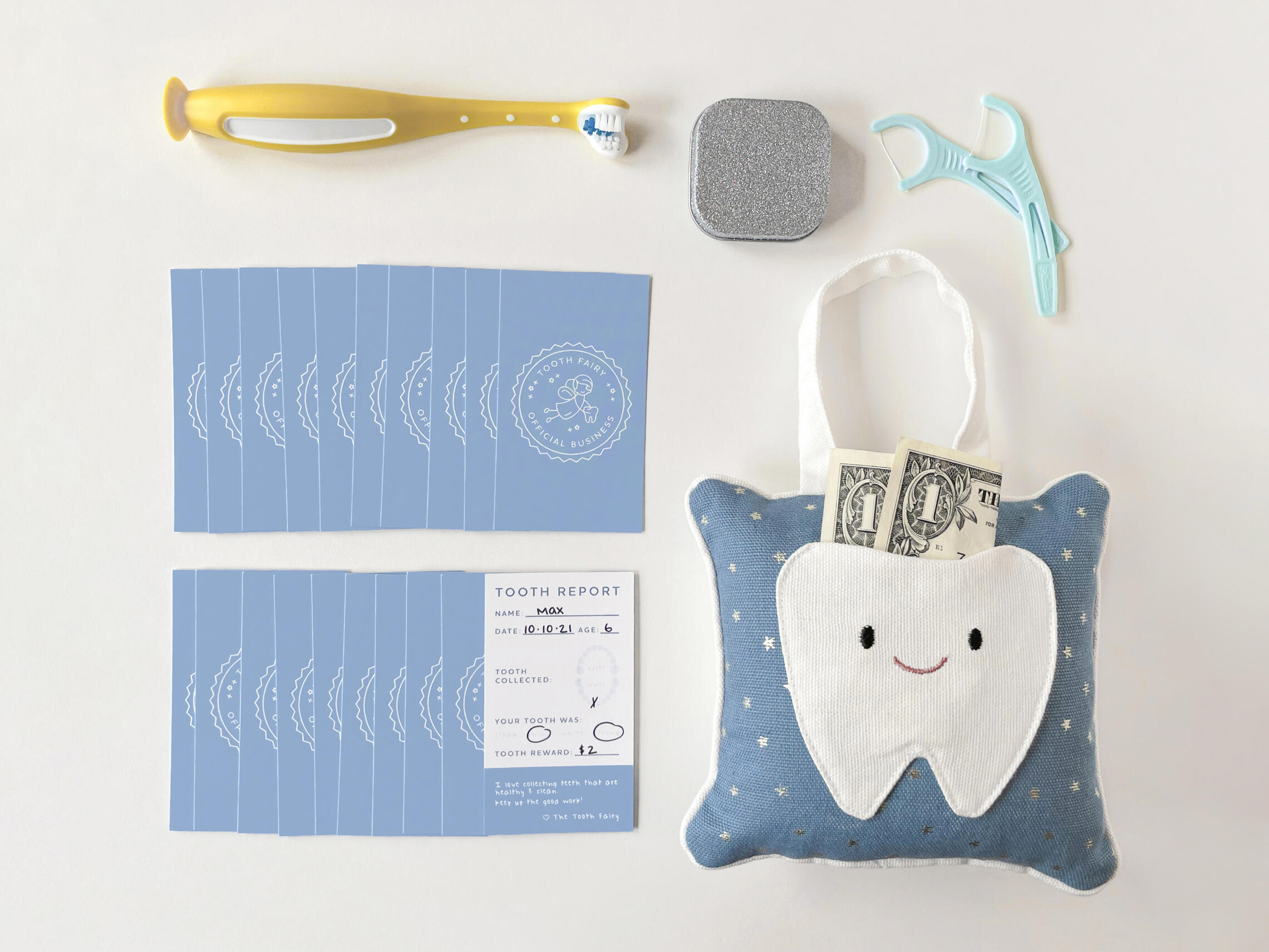 A flatlay image showing the tooth fairy cards along with several props on a white background. The props include a toothbrush, flosser picks, and a tooth fairy pillow.